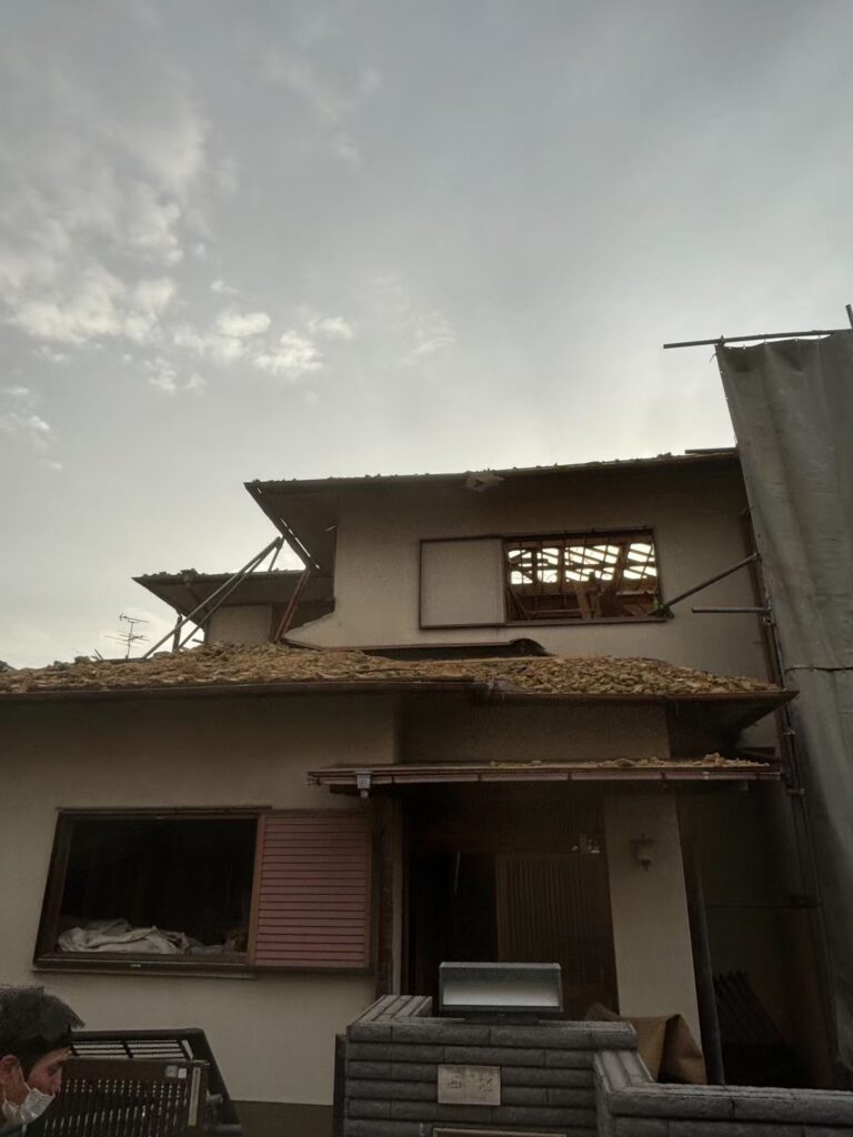 屋根解体が進み、内部構造が見える状態となった木造住宅の外観①